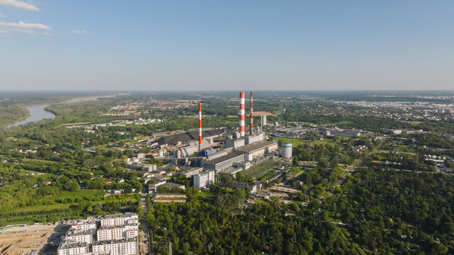 Aerial view of the Siekierki Power Station with its iconic red and white striped chimneys surrounded by lush greenery and urban infrastructure in Warsaw, Masovian Voivodeship, Poland.