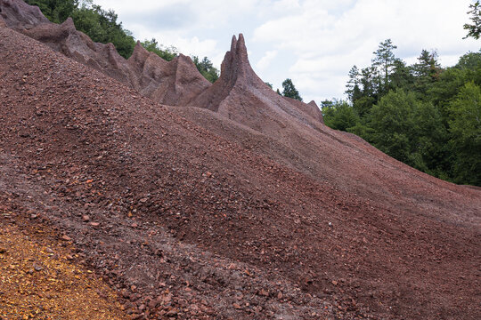 Sharp red mineral hills and barren gravel slopes rise against a cloudy sky at Le Roste di Montieri. These dramatic badlands reveal the intense geological impact of ancient industrial mining heritage.