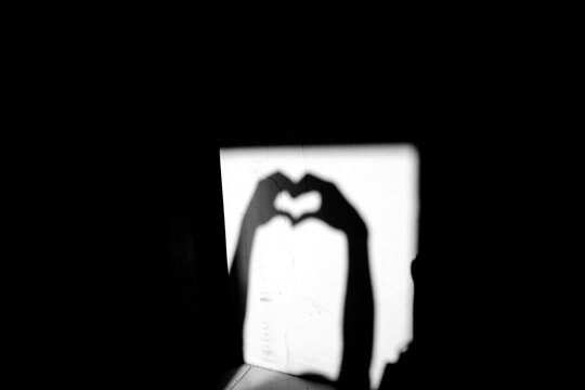 Close up black and white shadow of heart shape hand gesture on the dirty wall