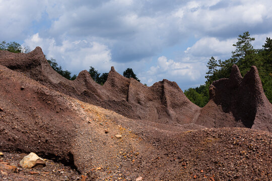 Eroded red mineral hills rise sharply under a bright cloudy sky at Le Roste di Montieri. These striking landscapes reveal the raw industrial heritage and powerful geological history of Tuscany.