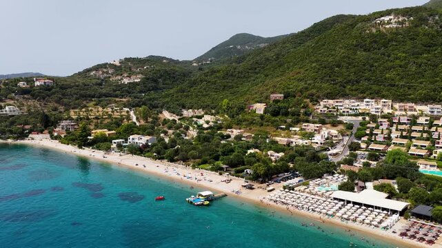 erial drone view of Barbati pebble beach and clear turquoise water, surrounded by green mountain slopes and summer resort villas on Corfu island in the Ionian Sea, Greece