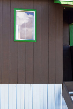 A close-up architectural view of a wooden upper wall, corrugated metal siding, and a green‑framed window