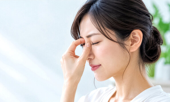 目を閉じて眉間を押さえる疲れた表情の女性