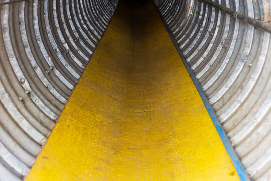 A cylindrical tunnel made of corrugated metal panels features a bright yellow floor and repeating concentric rings, creating strong symmetry and industrial depth