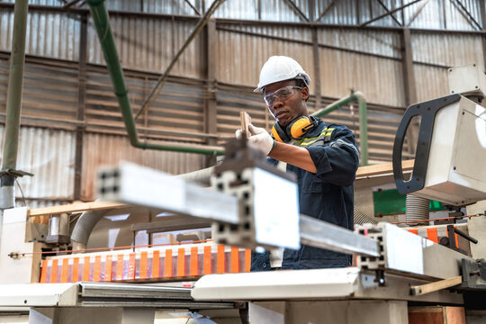 Black male quality control inspector verifying checks the length, width, and overall specifications of cut wood panels in timber manufacturing plant against custom client order requirements 
