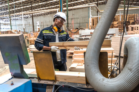 Black male quality control inspector verifying checks the length, width, and overall specifications of cut wood panels in timber manufacturing plant against custom client order requirements 