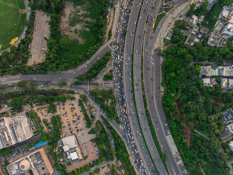Aerial view of a busy highway interchange with heavy traffic, surrounded by lush green trees and urban infrastructure in Gurgaon, Haryana, India.