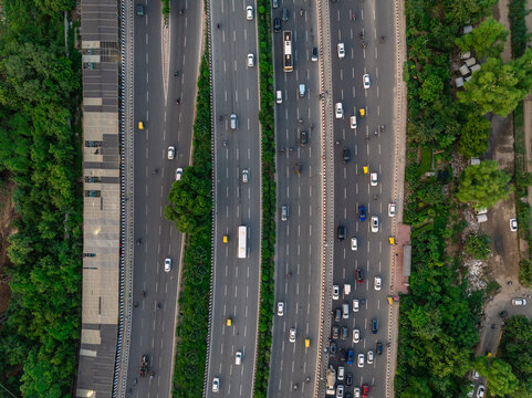 Aerial view of a busy multi-lane highway with cars and trucks driving through lush green surroundings in Gurgaon, Haryana, India.