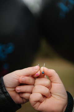 Closeup. Children hands holding sharp pins to pop black gender reveal balloons for twins outdoors.