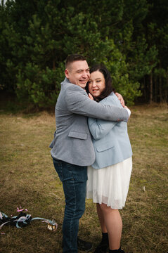 Happy couple embracing and smiling warmly outdoors in a forest during a twin gender reveal photo session.
