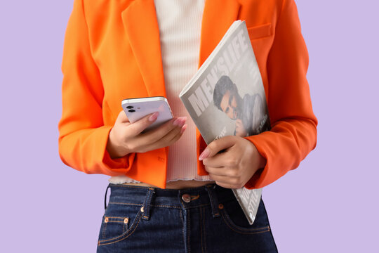 Beautiful young Asian woman with mobile phone and magazine on purple background