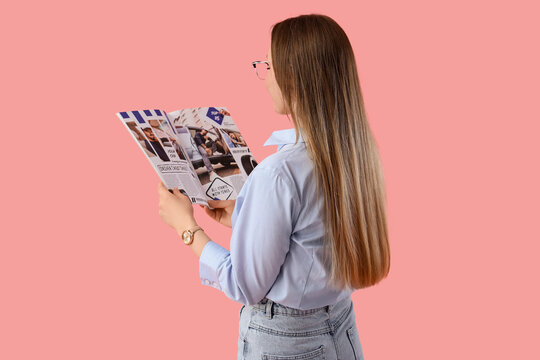 Beautiful young woman in eyeglasses reading magazine on pink background