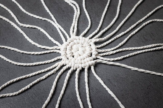 White macrame изделие with trailing cords on a dark background, elegant craft.