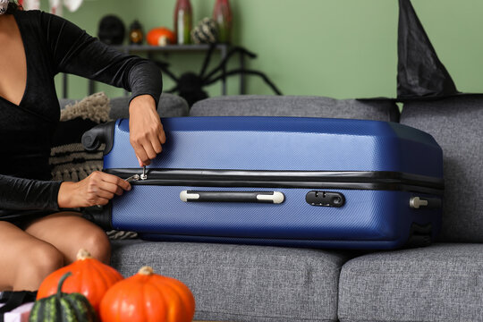 Female tourist dressed for Halloween unzipping suitcase at home, closeup