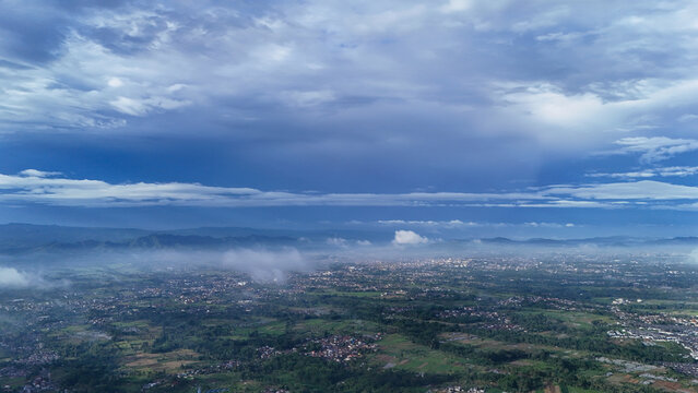 Aerial view of the landscape in Sukabumi Regency with lush greenery, scattered buildings, and distant mountains under a cloudy sky in Sukabumi Regency, West Java, Indonesia.