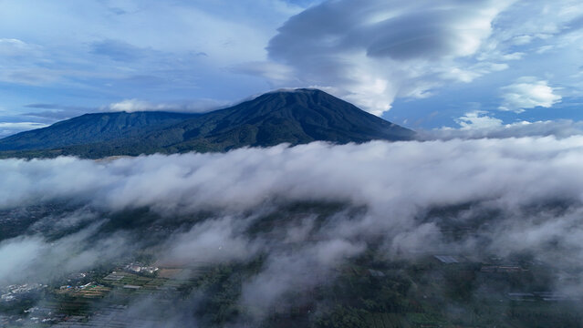 Aerial view of Gunung Gede Pangrango National Park rising above a thick layer of clouds with lush green mountain slopes and agricultural fields in Sukabumi, West Java, Indonesia.