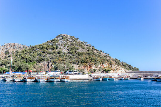 demre, Turkey - Numerous boats docked at a sunny coastal harbor with a rocky green hill in the background under a clear blue sky