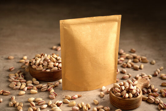 Blank craft paper zipper pouch packaging mockup surrounded by roasted salted pistachios on stone background