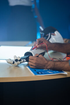 A person uses a multimeter to test the circuits of a robotic arm prototype on a table in a modern laboratory, focusing on engineering work and technical innovation.