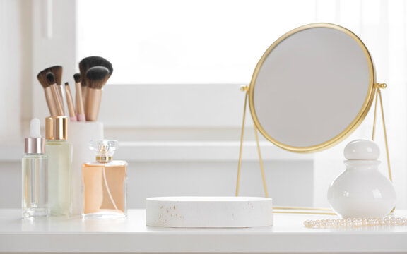 Elegant beauty vanity setup with empty stone podium, makeup brushes, perfume bottles, and gold mirror