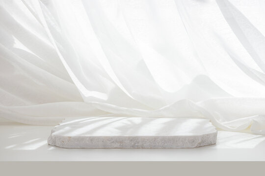 White empty marble podium in dappled sunlight on table with elegant draped curtain fabric background