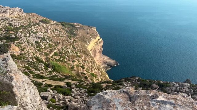 Panoramic view from the Dingli Cliffs in Malta, overlooking rugged limestone cliffs and the deep blue Mediterranean Sea. Scenic coastal landscape on a sunny summer day.