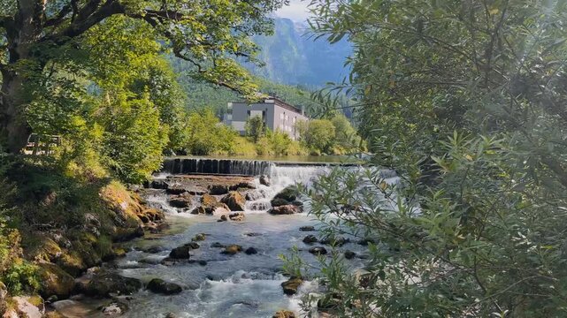 Scenic mountain river with rushing rapids and small cascades in Lofer, Austria, surrounded by lush green forest and Alpine mountains. Peaceful summer nature landscape with flowing water