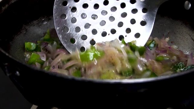 Stir frying chopped onion and capsicum in a pan.