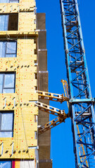 Modern building construction showing exterior insulation installation, facade work and tower crane operations during urban development © belavinstock