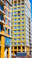 Large residential building under construction with installed windows, exterior insulation panels and unfinished facade elements during development © belavinstock