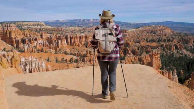 Female hiker with trekking poles and backpack walking along trail to scenic overlook in bryce canyon national park. Active tourist admiring the stunning red rock formations of the amphitheater