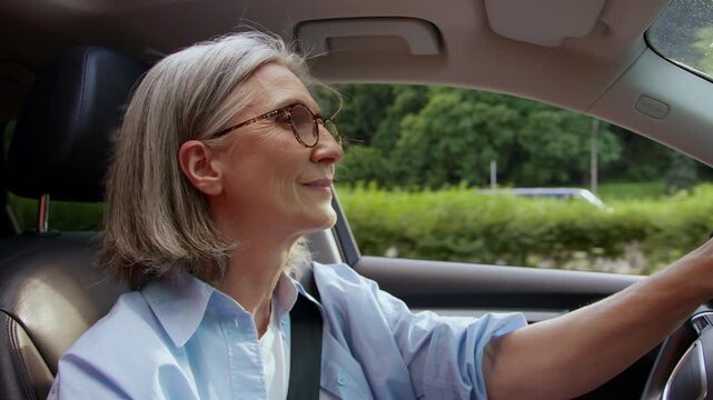 Happy retiree Caucasian senior mature woman driving car solo trip travel aged old female pensioner in glasses drive in automobile leasing modern auto steering wheel renting service transport insurance
