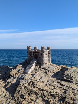 Miniature stone fortress model Castillo del Buho, perched on a rocky coastal cliff overlooking the blue sea in Andalusia, Spain