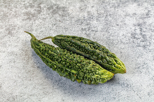 Two fresh green bitter melons with textured skin on light gray stone surface, natural lighting, shallow depth of field