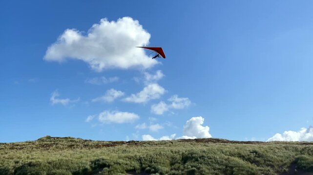 Paraglider bei einem Flug &uuml;ber D&uuml;nen am Strand an einem Sommertag mit blauem Himmel