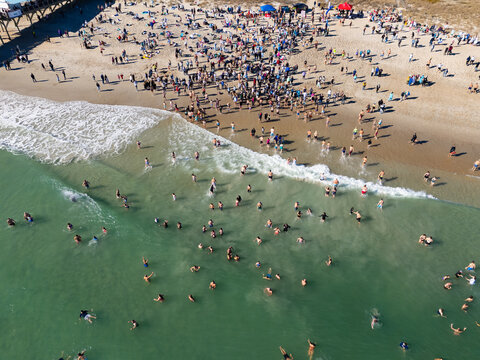 Aerial view of the annual Polar Plunge event at Crystal Pier with a large crowd of people entering the cold ocean water at Wrightsville Beach, North Carolina, United States.
