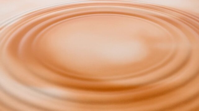 Concentric ripples expanding across a warm amber liquid surface in an abstract close view