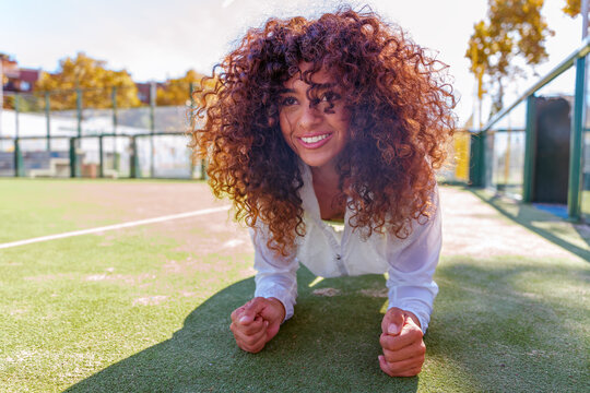 Smiling woman doing plank exercise on outdoor court, demonstrating strength, fitness, and healthy lifestyle