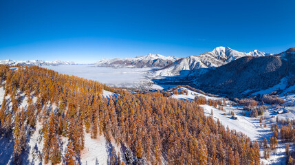 Aerial autumn view of the Champsaur Valley in the French Alps, with golden larch forest and snow-capped mountains. Ancelle, Hautes-Alpes, France