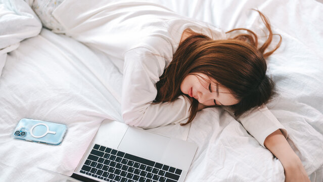 Young adult asian woman using laptop on bed for telemedicine mental health, online digital social network. People rest in cozy bedroom lying in bed