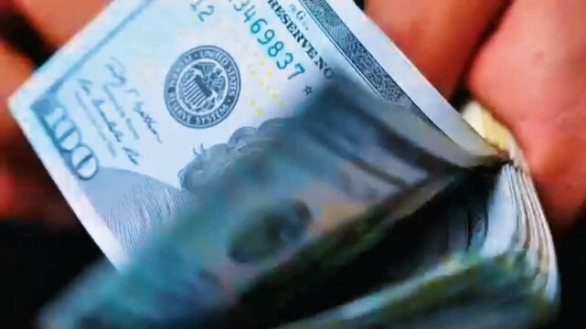 Macro extreme close up of hands rapidly fanning through thick stack of US dollar bills. Fast motion cash counting closeup video showcasing wealth, financial success, luxury and big money.