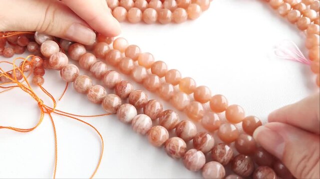 Faceted orange gemstone beads displaying shimmering mineral inclusions and polished surfaces arranged across multiple parallel threads for artisan jewelry projects