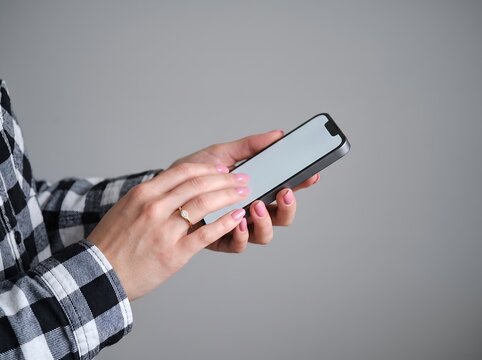 Hands Holding Blank-Screen Smartphone Against Gray Background