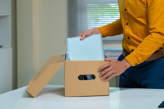 Closeup Businessman Packing Personal Belongings into Cardboard Box After Resignation or Job Termination in Office