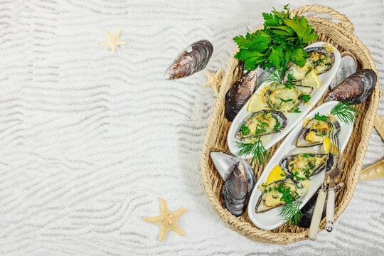 Baked mussels with cheese, herbs, and lemon served in a wicker tray on a sandy background