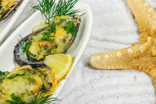 Baked mussels with melted cheese, dill, and lemon served on ceramic plate, white sand background