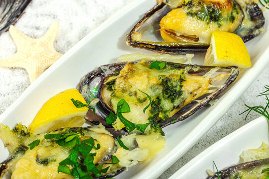 Baked mussels with melted cheese, dill, and lemon served on ceramic plate, white sand background