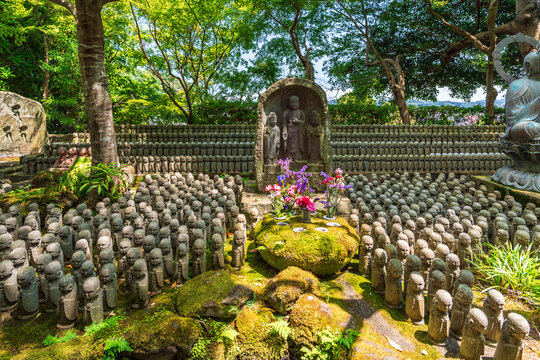 Stone Jizo statues and flowers in lush garden at Hase-dera temple in Kamakura Japan