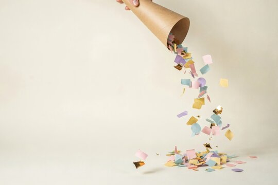 Pastel confetti pouring from a kraft paper cone onto a cream background