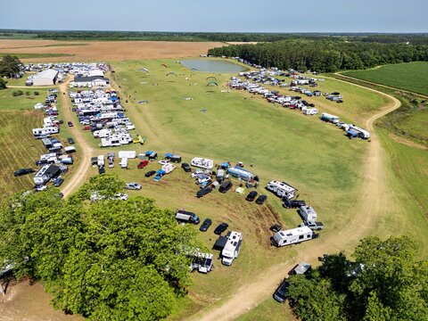 Aerial view of the Bad Apples PPG fly-in at Hodges Field, with recreational vehicles, paragliders, and a small pond in the grassy fields of Andersonville, Georgia, United States.